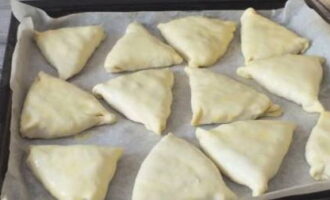 Plaats de gevormde samsa op een bakplaat met bakpapier, met de naad naar beneden, en bestrijk met losgeklopt ei om hem goudbruin te maken. Bak gedurende 20-25 minuten op 180 graden.
