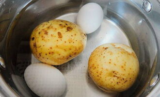 În același timp, fierbeți cartofii spălați în jachete. Fierbe tare ouăle de găină. Răciți rapid ingredientele fierte în apă rece.