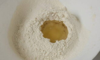 Aboqueu la farina tamisada en un bol per pastar la massa o sobre el taulell i salpebreu.Feu una depressió al mig d'aquesta diapositiva i aboqueu-hi oli vegetal inodor. 