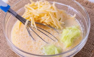 Alisan ng tubig ang mas maraming juice hangga't maaari mula sa masa ng zucchini. Ilagay ang ginutay-gutay na keso dito at ibuhos ang pinaghalong itlog-gatas. Paghaluin muli ang lahat ng mabuti gamit ang isang whisk.