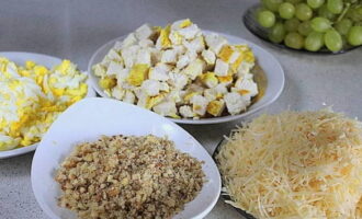 Gupitin ang pinalamig na fillet sa maliliit na cubes. Gilingin ang pinakuluang itlog at keso sa isang magaspang na kudkuran. Gilingin ang mga mani sa medium crumbs gamit ang isang blender. Paghiwalayin ang mga ubas mula sa bungkos, gupitin sa kalahati at alisin ang mga buto. Sa isang tasa, ihalo ang mayonesa sa yogurt.