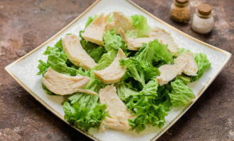 Maghanda ng isang ulam kung saan kokolektahin mo ang salad. Banlawan at tuyo ang mga dahon ng litsugas. Maglagay ng ulam at ilagay sa ibabaw ang tinadtad na hiwa ng manok.