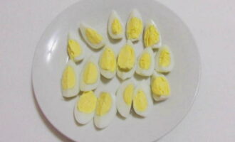 Balatan ang pinakuluang at pinalamig na mga itlog ng pugo at gupitin sa apat na bahagi.