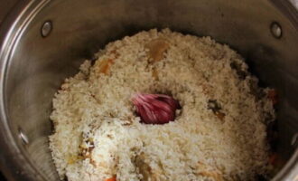 Giet rijst in de pan. Verdeel het gelijkmatig. Bestrooi met kruiden voor pilaf en steek een kop knoflook in het midden, waarvan we eerst de bovenste schil verwijderen.