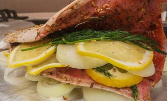 Lägg den beredda fisken ovanpå. Inuti slaktkroppen placerar vi flera bitar av lök och citron och en kvist dill.