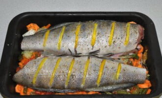 Lägg grönsakerna i en ugnsform. Lägg fisken ovanpå. Vi gör snitt och fyller dem med tunna citronskivor.