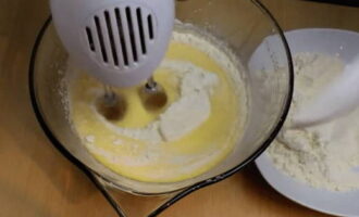 Cerneți făina într-o sită. Fără a opri mixerul, turnăm făina în ouăle bătute în porții și frământăm aluatul până se omogenizează. Porniți cuptorul la 180°C.