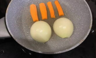 Curata morcovii folosind o menajera. Scoateți pielea de pe bulbi. Tăiați morcovii în 4 părți și o ceapă în jumătate. Pune legumele preparate pe o tigaie fierbinte.