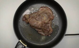 Verhit de koekenpan. Leg het vlees op hoog vuur bruin en sluit de vleessappen binnenin af. Verwijder het vlees. Voeg hier gehakte uien, knoflook en aromatische kruiden toe. Sauteer tot het transparant is.