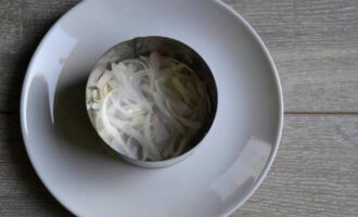 Alisan ng tubig ang sibuyas sa pamamagitan ng isang salaan. Iwanan upang hayaang maubos ang likido. Maglagay ng cooking ring sa plato para sa pag-assemble ng salad. Bumuo ng unang layer ng mga sibuyas.