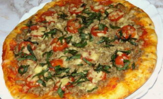La pizza amb carn picada, formatge i tomàquet està llesta al forn. Decoreu amb herbes i serviu!