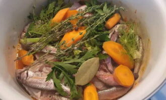 Așezați peștele mic, capetele și țepii deasupra legumelor. Morcovii se toaca grosier si se adauga in tigaie. Adăugați acolo foi de dafin, boabe de piper, cimbru și verdeață de fenicul. Asezonați generos cu sare.