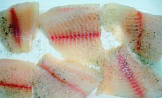 Clătiți fileurile de tilapia dezghețate cu apă rece, uscați cu un șervețel și tăiați în bucăți. Puneți tilapia feliată pe o farfurie plată și presărați cu sare și piper negru după gust. Lăsați tilapia la marinat timp de 10 minute.