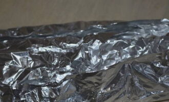 Inilalagay namin ang workpiece sa isang sheet ng foil, ilagay ang natitirang mga sibuyas sa itaas - balutin ito sa foil.