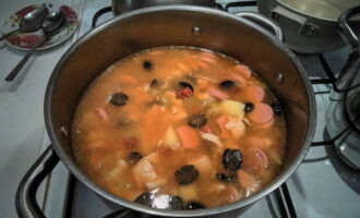 Cho khoai tây cắt nhỏ vào nước luộc gà và nấu cho đến khi mềm. Sau đó thêm rau hầm, xúc xích thái lát, thịt gà và ô liu vào.