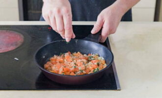 Tillsätt tomatbitar och hackad basilika till löken. Salta innehållet och strö över malen svartpeppar. Sjud grönsakerna tills vätskan avdunstat.