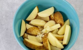 No peleu les patates. Talleu els tubercles a rodanxes fines i poseu-los en un bol gran. Peleu els grans d'all, passeu-los per una premsa i afegiu-hi la polpa resultant al bol amb les patates.