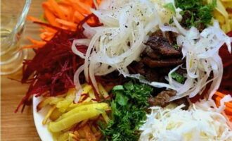 Puneți alimentele pregătite în grămezi pe un vas plat de servire, inclusiv carne și cartofi. Stoarceți umezeala din ceapă și puneți-o deasupra ingredientelor, adăugați căței de usturoi și ierburi, turnați ulei vegetal și salata este gata. Hai să gustăm!