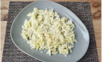 Skala potatisen, hacka den på ett grovt rivjärn, lägg den i första lagret på en bred salladsskål och strö över salt och svartpeppar.