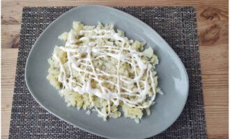 Täck potatisskiktet med ett tunt nät av majonnäs.