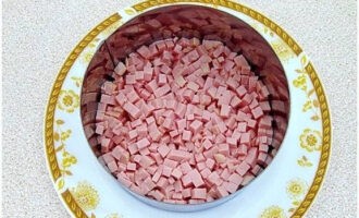 A salátát karika segítségével formázzuk. Az első rétegbe helyezzük a kolbászt.
