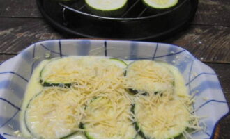 Ibuhos ang isang maliit na sarsa sa ilalim ng baking dish. Ilagay ang ilan sa mga bilog ng zucchini, ibuhos muli ang sarsa at iwiwisik ang gadgad na keso.