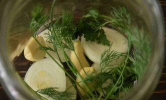 Col·loqueu les herbes, els grans d'all i els trossos de ceba al fons dels pots preparats.