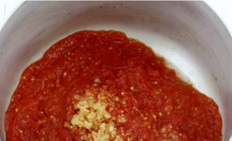 Ang pagbibihis para sa sopas para sa taglamig sa mga garapon ay medyo simple upang ihanda - magsimula tayo! Ipasa ang mga makatas na kamatis at peeled na bawang sa pamamagitan ng grill ng isang gilingan ng karne, ibuhos ang pulp sa isang malaking kasirola.