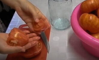 Alisan ng tubig ang mainit na tubig. Maingat na alisin ang alisan ng balat mula sa bawat kamatis mula sa base ng tangkay, gupitin sa mga hiwa depende sa laki at ilagay nang siksik sa malinis na mga garapon ng litro.