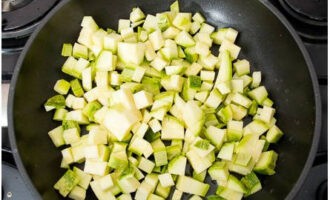 Esbandiu el carbassó amb aigua, talleu-lo a daus i tireu-ne un tercer en una paella amb oli vegetal. 
