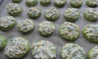 Col·loqueu els cercles de carbassó en una safata de forn folrada amb pergamí. Cobriu-los amb la barreja de formatge.