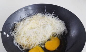 Låt risnudlarna rinna av. Lägg den sedan i en wok och bryt kycklingäggen. När äggen stelnat lite, rör ner dem i nudlarna.