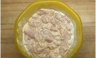 Cartofii cu pui și ciuperci la cuptor se prepară rapid și ușor. Clătiți fileul de pui cu apă rece, tăiați cubulețe mici și puneți într-un castron separat. Se presară cu sare și condimente, se adaugă trei linguri de smântână, se amestecă și se lasă 15-20 de minute la marinat.