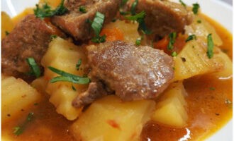 Ang nilagang patatas na may karne sa isang kaldero sa kalan ay handa na. Ilagay sa mga plato at itaas na may mga damo!