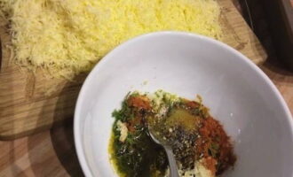 Meng in een kom de knoflook, door een pers gehaald, fijngehakte dille, olijfolie, paprika, zwarte peper en zout. Ook raspen we de kaas met een fijne rasp.