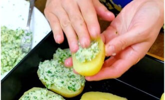 Col·loqueu les patates a la meitat en una safata de forn untada. Repartim el farcit fragant per sobre.