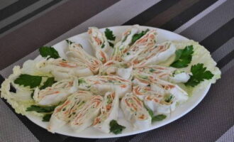 Lavash fylld med ostmassa och röd fisk är klar. Skär aptitretaren och lägg den på en tallrik med kinakålsblad, garnerade med färska örter.