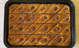 Efter att ha tagit ut den färdiga baklavan uppdaterar vi slitsarna och häller sirap över varje diamant. När desserten har svalnat helt, gör du snitt ända ner till botten.
