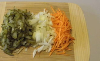 Nang walang pag-aaksaya ng oras, ihanda ang dressing: gupitin ang mga adobo na mga pipino at mga peeled na sibuyas sa mga cube, at i-chop ang mga karot gamit ang isang borage grater.
