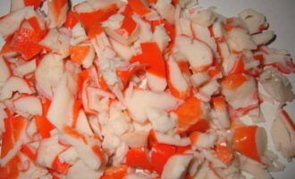 Gupitin ang ganap na na-defrost na karne ng alimango o mga stick sa mga cube at ilagay din sa isang mangkok ng salad.Hindi na kailangang i-chop ito ng masyadong maliit - gupitin ito sa mga medium cubes. Upang mabilis na mag-defrost ng crab sticks, ilagay lamang ang mga ito sa isang mangkok ng tubig sa loob ng ilang minuto.