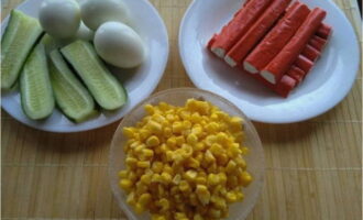 Hoe maak je een salade met krabsticks, maïs, ei en komkommer volgens het klassieke recept? Kook en schil kippeneieren, laat de pekel uit de maïs lopen en spoel de komkommers.
