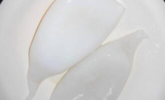 Hoe maak je een salade met inktvis- en krabsticks klaar? Ontdooi de inktviskarkassen en was ze. Het is belangrijk om alle films te verwijderen.