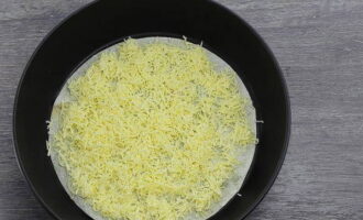 เราขูดชีสแข็งบนเครื่องขูดที่มีรูขนาดกลางแล้วโรยเศษชีสครึ่งหนึ่งบนฐาน lavash