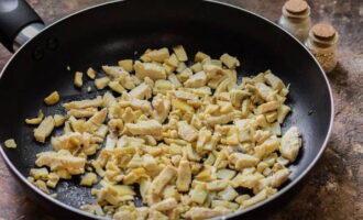 Uscați tigaia la foc mare, turnați ulei vegetal în ea, distribuiți-l pe toată suprafața. Mai întâi, prăjiți feliile de ciuperci timp de 2-3 minute. Dupa aceasta adaugam carnea de pui tocata anterior si continuam sa prajim totul impreuna inca 3-4 minute, amestecand din cand in cand ciupercile si puiul cu o spatula. Produsele trebuie să fie ușor rumenite.